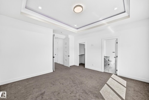 Tray ceiling with recessed lighting and a central flush-mount fixture, soft gray carpeting, and white interior doors with black hardware - 3101 Soleil Boulevard, Beaumont, AB - Indoor Photo Showing Other Room