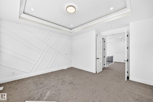 Tray ceiling with recessed lighting and a central flush-mount fixture, geometric accent wall, and gray carpet flooring - 3101 Soleil Boulevard, Beaumont, AB - Indoor Photo Showing Other Room