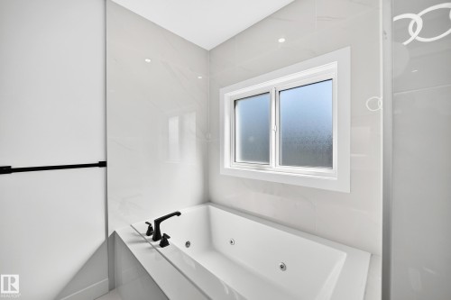 Built-in tub with matte black fixtures, white window frame, and tiled surround - 3101 Soleil Boulevard, Beaumont, AB - Indoor Photo Showing Bathroom