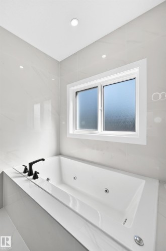 Recessed lighting, tiled walls, jetted soaking tub, matte black fixtures, and a white framed window with obscured glass - 3101 Soleil Boulevard, Beaumont, AB - Indoor Photo Showing Bathroom