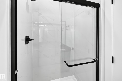 Glass-enclosed shower with matte black framing, clear glass panels, matte black door pull, and white tiled walls with subtle veining - 3101 Soleil Boulevard, Beaumont, AB - Indoor Photo Showing Bathroom
