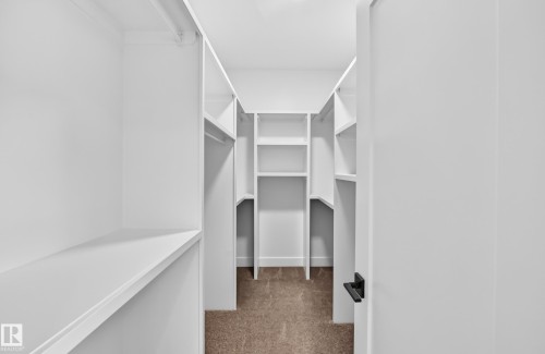 Walk-in closet with built-in shelving, hanging rods, light brown carpet, and a white interior - 3101 Soleil Boulevard, Beaumont, AB - Indoor With Storage