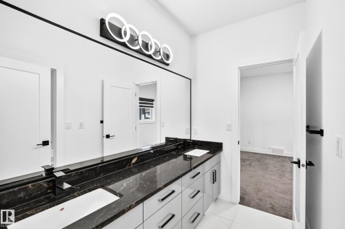Double vanity with a dark polished countertop, dual undermount sinks, and contemporary light fixture - 3101 Soleil Boulevard, Beaumont, AB - Indoor