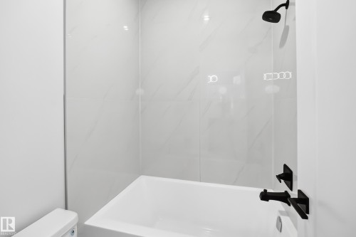 Bathtub with matte black fixtures, white tile surround, and an integrated shower head - 3101 Soleil Boulevard, Beaumont, AB - Indoor Photo Showing Bathroom