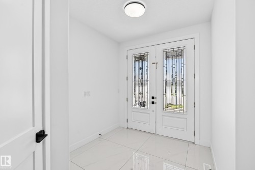 Double entry doors with decorative glass panels, white tile flooring, and a flush-mount ceiling light fixture - 3101 Soleil Boulevard, Beaumont, AB - Indoor Photo Showing Other Room