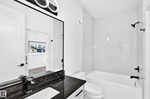 Black countertop with integrated sink, black hardware throughout, modern vanity lighting, white subway tile shower surround, and a white bathtub - 3101 Soleil Boulevard, Beaumont, AB - Indoor Photo Showing Bathroom