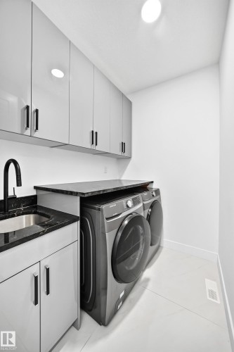 Built-in laundry sink with dark countertop, light grey cabinetry, and overhead storage - 3101 Soleil Boulevard, Beaumont, AB - Indoor Photo Showing Laundry Room