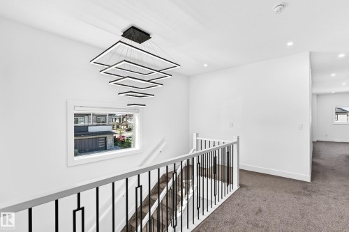 Modern tiered geometric chandelier, white painted walls, window with white trim, black and white staircase railing, and grey carpeting - 3101 Soleil Boulevard, Beaumont, AB - Indoor Photo Showing Other Room