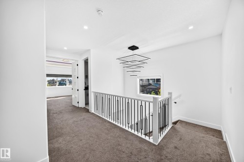 Contemporary multi-tier chandelier, sleek metal stair railing, recessed lighting, and white trim - 3101 Soleil Boulevard, Beaumont, AB - Indoor Photo Showing Other Room