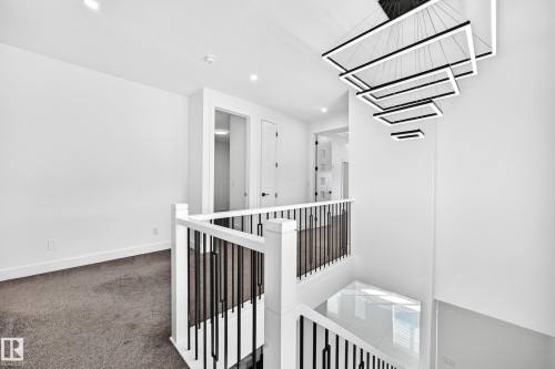 Contemporary tiered chandelier, recessed lighting, white walls, and dark carpet - 3101 Soleil Boulevard, Beaumont, AB - Indoor Photo Showing Other Room