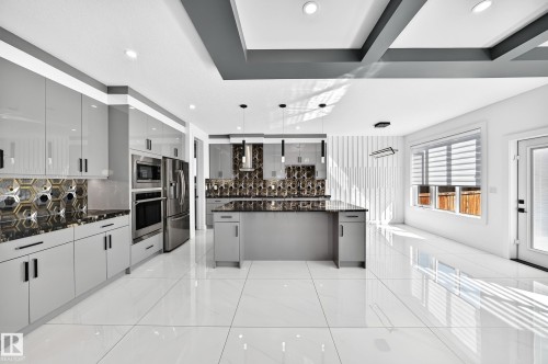 Gleaming white large format tile flooring, contemporary kitchen island with dark stone countertop, full suite of stainless steel appliances, modern gray cabinetry, and recessed ceiling lighting - 3101 Soleil Boulevard, Beaumont, AB - Indoor Photo Showing Kitchen With Upgraded Kitchen