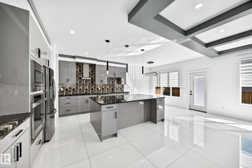White tile flooring, gray flat-panel cabinetry, stainless steel appliances, dark stone countertops, and a coffered ceiling - 3101 Soleil Boulevard, Beaumont, AB - Indoor Photo Showing Kitchen With Upgraded Kitchen