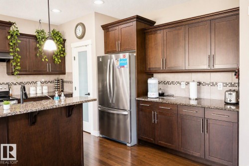 Kitchen featuring rich wood-finish cabinetry, speckled countertops, stainless steel appliances, and a tiled backsplash - 711 57 St Sw, Edmonton, AB - Indoor Photo Showing Kitchen