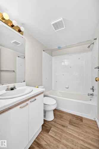 Bathroom featuring a white vanity with a laminate countertop, a drop-in sink, a standard toilet, a tub with a shower, and wood-finish flooring - #204 11218 80 St Nw, Edmonton, AB - Indoor Photo Showing Bathroom