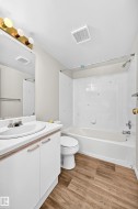 Bathroom featuring a white vanity with a laminate countertop, a drop-in sink, a standard toilet, a tub with a shower, and wood-finish flooring - 