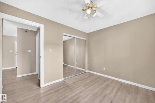 Wood-finish flooring, mirrored closet doors, ceiling fan with integrated lighting, and neutral wall tones - #204 11218 80 St Nw, Edmonton, AB - Indoor Photo Showing Other Room