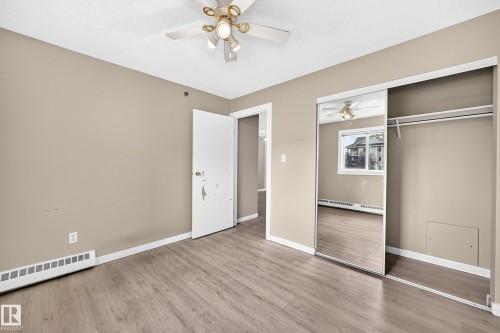 Wood-finish flooring, ceiling fan, mirrored closet doors, and built-in closet rod - #204 11218 80 St Nw, Edmonton, AB - Indoor Photo Showing Other Room