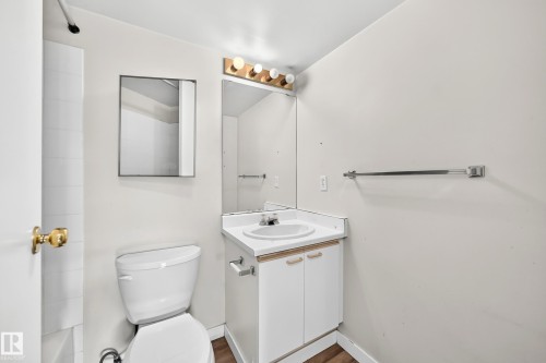 Integrated vanity with white countertop and sink, wall-mounted mirror, and wood-finish flooring - #204 11218 80 St Nw, Edmonton, AB - Indoor Photo Showing Bathroom