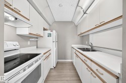 Galley kitchen featuring wood-finish flooring, white cabinetry with wood trim, white countertops, a double basin stainless steel sink, and a white electric range - 