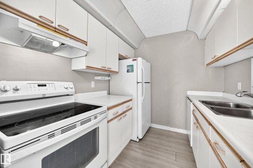 White cabinetry with wood-finish trim, stainless steel double basin sink, and wood-finish flooring - #204 11218 80 St Nw, Edmonton, AB - Indoor Photo Showing Kitchen With Double Sink