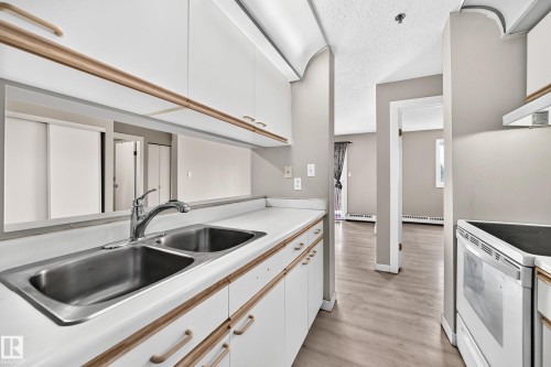 Kitchen featuring a dual basin stainless steel sink, white cabinetry with wood-finish trim, and white laminate countertops - #204 11218 80 St Nw, Edmonton, AB - Indoor Photo Showing Kitchen With Double Sink