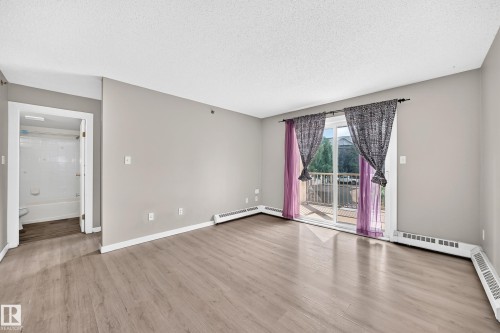 Light gray wall paint, wood-finish flooring, sliding glass door, white trim, and a full bathroom with a white tub - #204 11218 80 St Nw, Edmonton, AB - Indoor Photo Showing Other Room