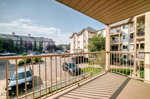 Expansive balcony with a textured floor and painted metal railing, overlooking a parking area and multiple building exteriors - #204 11218 80 St Nw, Edmonton, AB - Outdoor With Balcony With Exterior