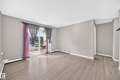 Spacious interior featuring wood-finish flooring, light neutral wall paint, and a sliding glass door - #204 11218 80 St Nw, Edmonton, AB - Indoor Photo Showing Other Room