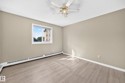 Wood-finish flooring, neutral wall paint, and a white ceiling fan with integrated lighting - #204 11218 80 St Nw, Edmonton, AB - Indoor Photo Showing Other Room