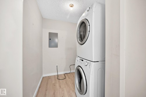 Stacked washer and dryer units, wood-finish flooring, and a flush-mount ceiling light - #204 11218 80 St Nw, Edmonton, AB - Indoor Photo Showing Laundry Room