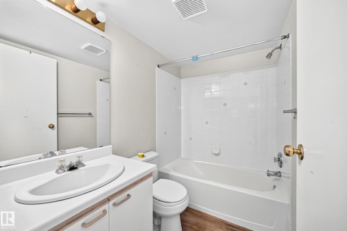 Bathroom featuring a white vanity with integrated sink, a large wall-mounted mirror, overhead vanity lighting, a full-sized bathtub with shower, and white tiled shower surround - #204 11218 80 St Nw, Edmonton, AB - Indoor Photo Showing Bathroom