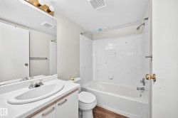 Bathroom featuring a white vanity with integrated sink, a large wall-mounted mirror, overhead vanity lighting, a full-sized bathtub with shower, and white tiled shower surround - 