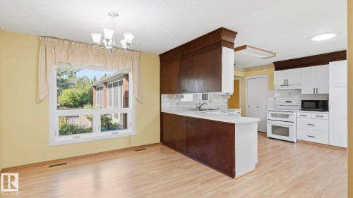 Wood-finish flooring, white kitchen cabinetry, white appliances, and a kitchen island with a white countertop - 8408 176 Street Nw, Edmonton, AB - Indoor Photo Showing Kitchen