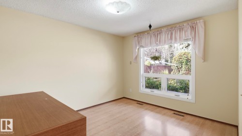 Hardwood-style flooring, neutral wall paint, and a large window with white trim - 8408 176 Street Nw, Edmonton, AB - Indoor Photo Showing Other Room