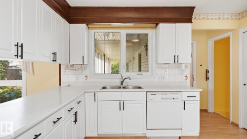 White cabinetry with matte black hardware, white countertops, built-in stainless steel sink, tile backsplash, and a white dishwasher - 8408 176 Street Nw, Edmonton, AB - Indoor Photo Showing Kitchen With Double Sink