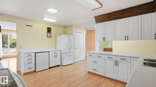 Kitchen featuring white cabinetry, light countertops, wood-finish flooring, and white appliances - 8408 176 Street Nw, Edmonton, AB - Indoor Photo Showing Kitchen With Double Sink