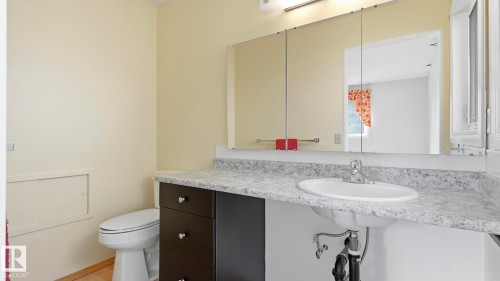 White oval sink with chrome faucet, dark wood-finish vanity, light-colored countertop, and wall-mounted mirror - 8408 176 Street Nw, Edmonton, AB - Indoor Photo Showing Bathroom