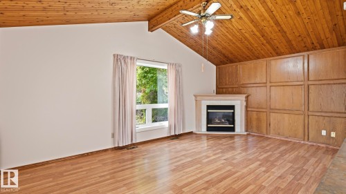 Vaulted wood-paneled ceiling, wood-finish flooring, corner fireplace with a mantel, wood-paneled accent wall, and a ceiling fan with integrated lighting - 8408 176 Street Nw, Edmonton, AB - Indoor Photo Showing Living Room With Fireplace