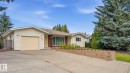 Exterior featuring light-colored siding, an attached garage, a concrete driveway, a stone retaining wall, and mature evergreen trees - 8408 176 Street Nw, Edmonton, AB  - Outdoor 