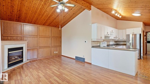 Vaulted wood-finish ceiling, wood-finish flooring, corner fireplace with mantel, paneled accent wall, and white kitchen cabinetry - 8408 176 Street Nw, Edmonton, AB - Indoor Photo Showing Kitchen With Fireplace