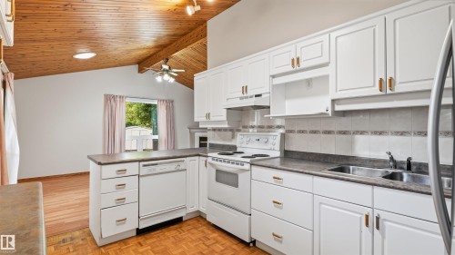 Vaulted wood-paneled ceiling, white cabinetry with gold-tone hardware, white appliances, and a double basin sink - 8408 176 Street Nw, Edmonton, AB - Indoor Photo Showing Kitchen With Double Sink