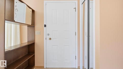 White paneled door with brass hardware, wood-finish shelving unit, and white bi-fold closet doors - 8408 176 Street Nw, Edmonton, AB - Indoor Photo Showing Other Room