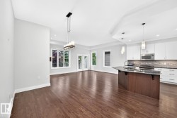 Hardwood flooring, kitchen island with dark stone countertop, white shaker-style cabinetry, stainless steel appliances, and contemporary pendant lighting - 