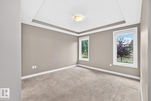 Tray ceiling with crown molding, two windows with white trim, light gray carpet, and a flush-mount ceiling light fixture - #57 18343 Lessard Rd Nw, Edmonton, AB - Indoor Photo Showing Other Room