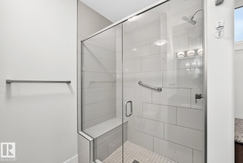 Glass-enclosed shower with a built-in bench, subway tile surround, rainfall shower head, and a chrome grab bar - #57 18343 Lessard Rd Nw, Edmonton, AB - Indoor Photo Showing Bathroom