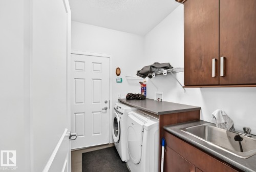 Laundry area featuring wood-finish cabinetry, a utility sink, and a work surface - #57 18343 Lessard Rd Nw, Edmonton, AB - Indoor Photo Showing Laundry Room