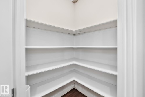 Corner pantry featuring three tiers of white shelving with clean lines and ample storage capacity - #57 18343 Lessard Rd Nw, Edmonton, AB - Indoor With Storage