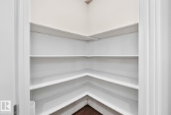 Corner pantry featuring three tiers of white shelving with clean lines and ample storage capacity - 