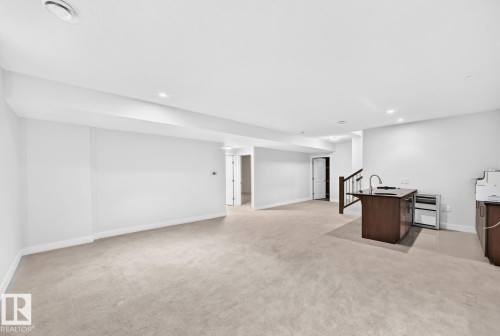 Recessed lighting illuminates the expansive carpeted area, featuring an integrated wet bar with wood-finish cabinetry and a dark countertop - #57 18343 Lessard Rd Nw, Edmonton, AB - Indoor Photo Showing Other Room