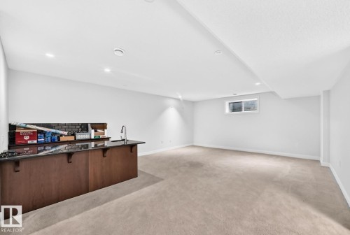 Spacious finished basement with recessed lighting, light-colored carpeting, and a built-in wet bar featuring a dark countertop and a stainless steel faucet - #57 18343 Lessard Rd Nw, Edmonton, AB - Indoor Photo Showing Other Room